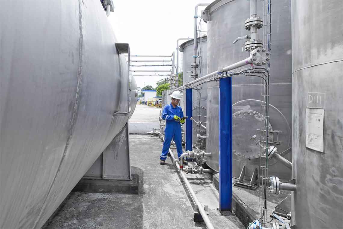 Person in blue coveralls, hard hat, and yellow gloves checki