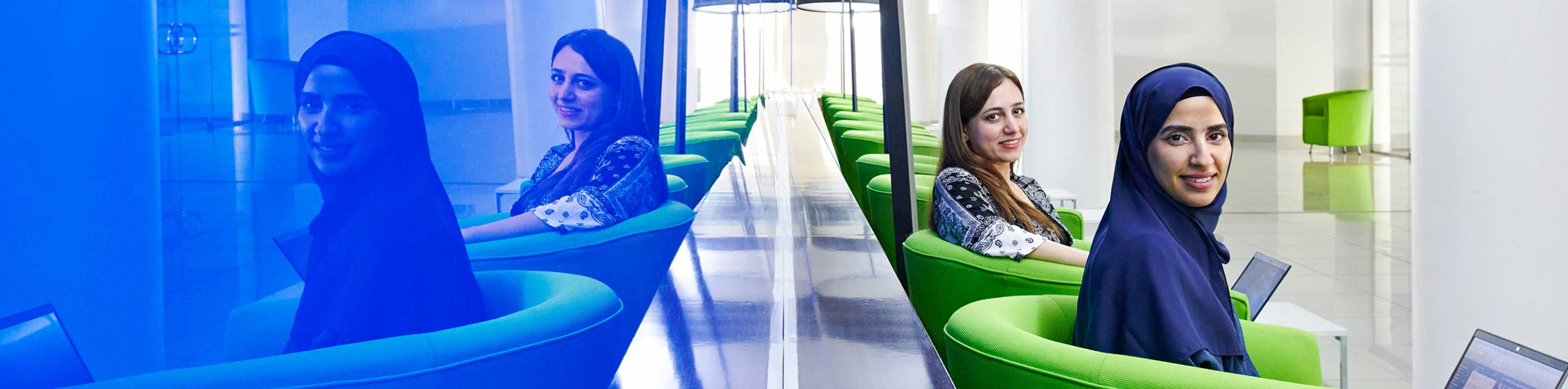 Two women sitting in lounge chairs with their reflections showing on a blue wall behind them